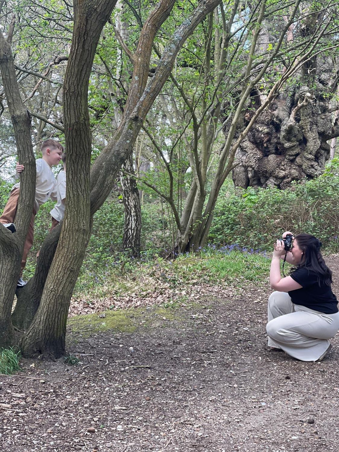 Simone crouching with her camera in the woods, photographing children in a tree