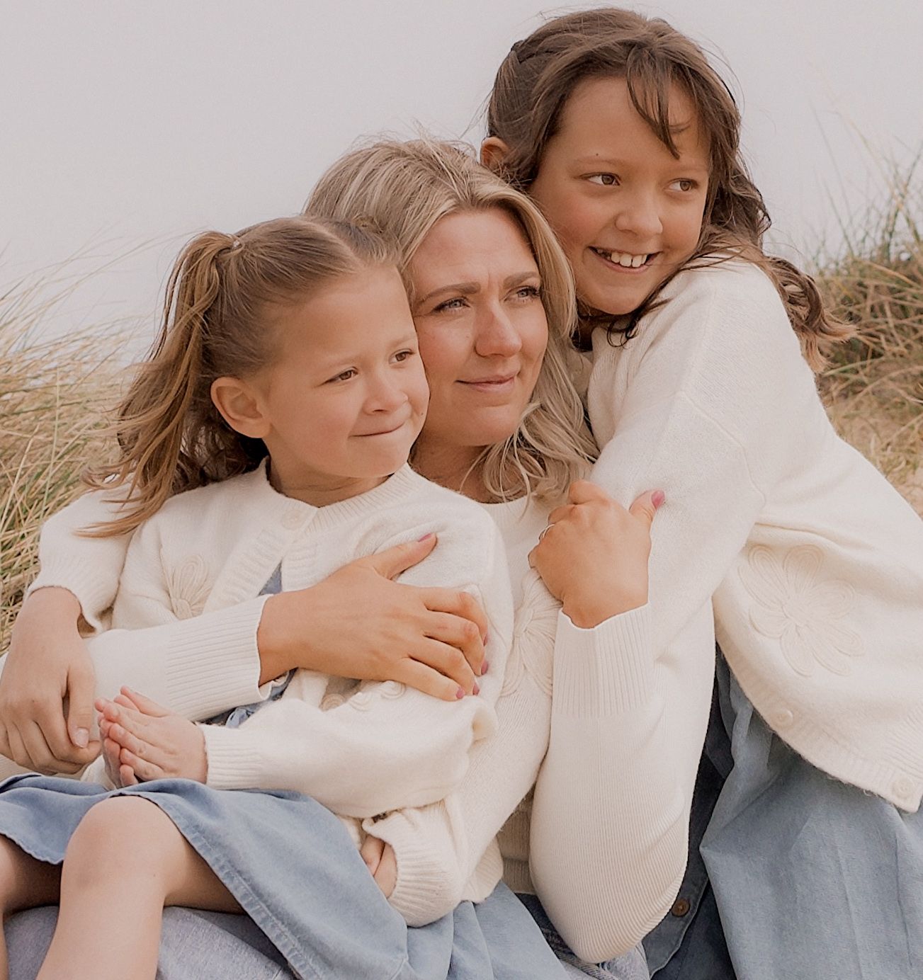 Mum hugging her two daughters in the sand dunes