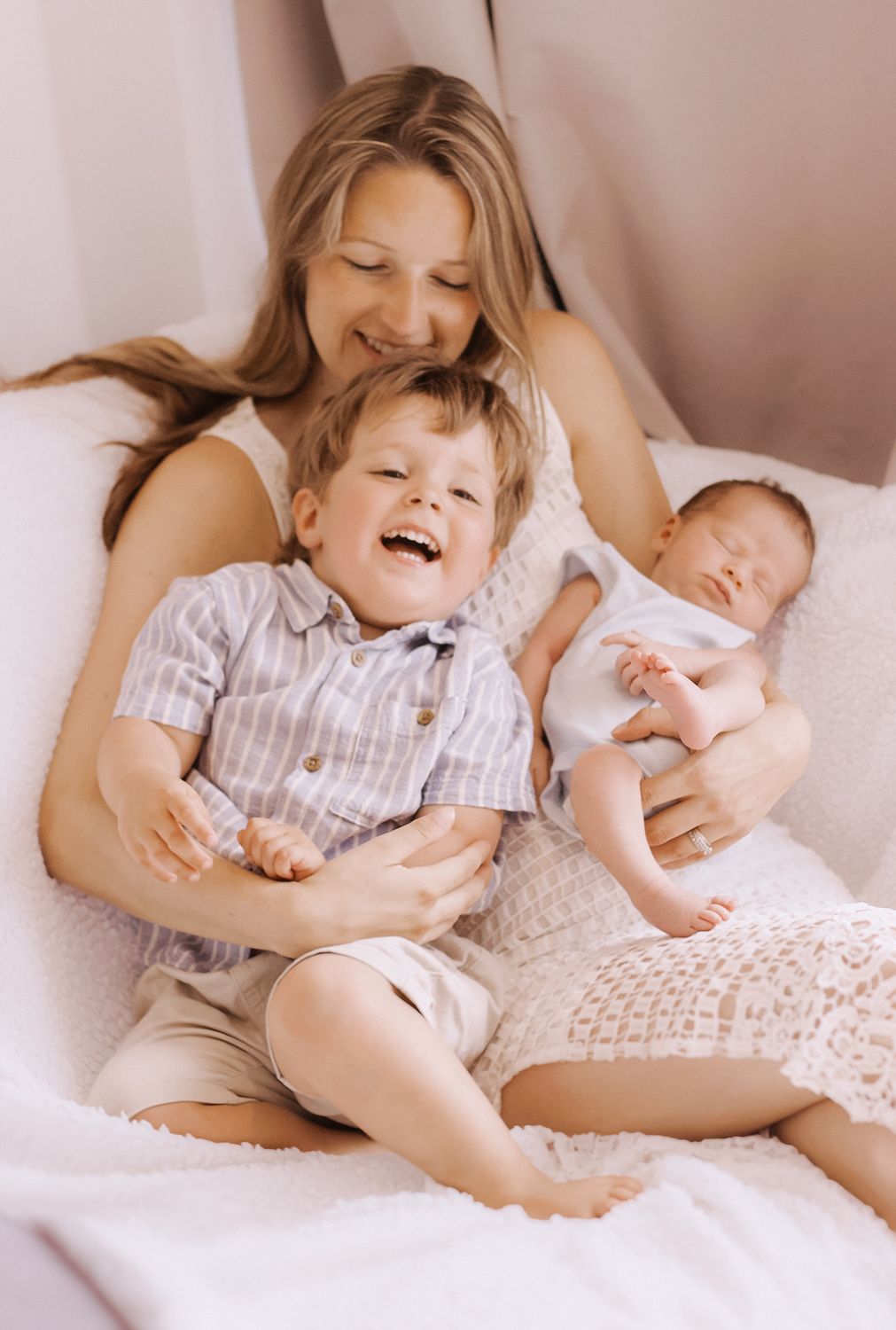 Mum laughing with her toddler and newborn on a bed