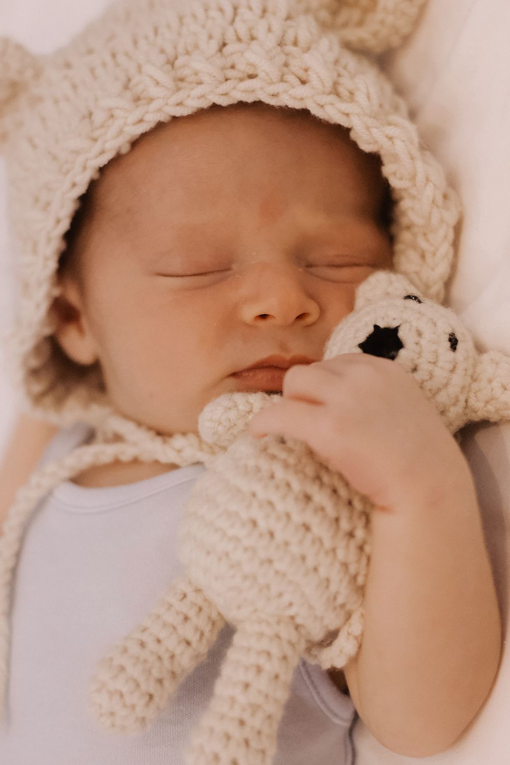 Sleeping newborn in a knitted bonnet holding a teddy