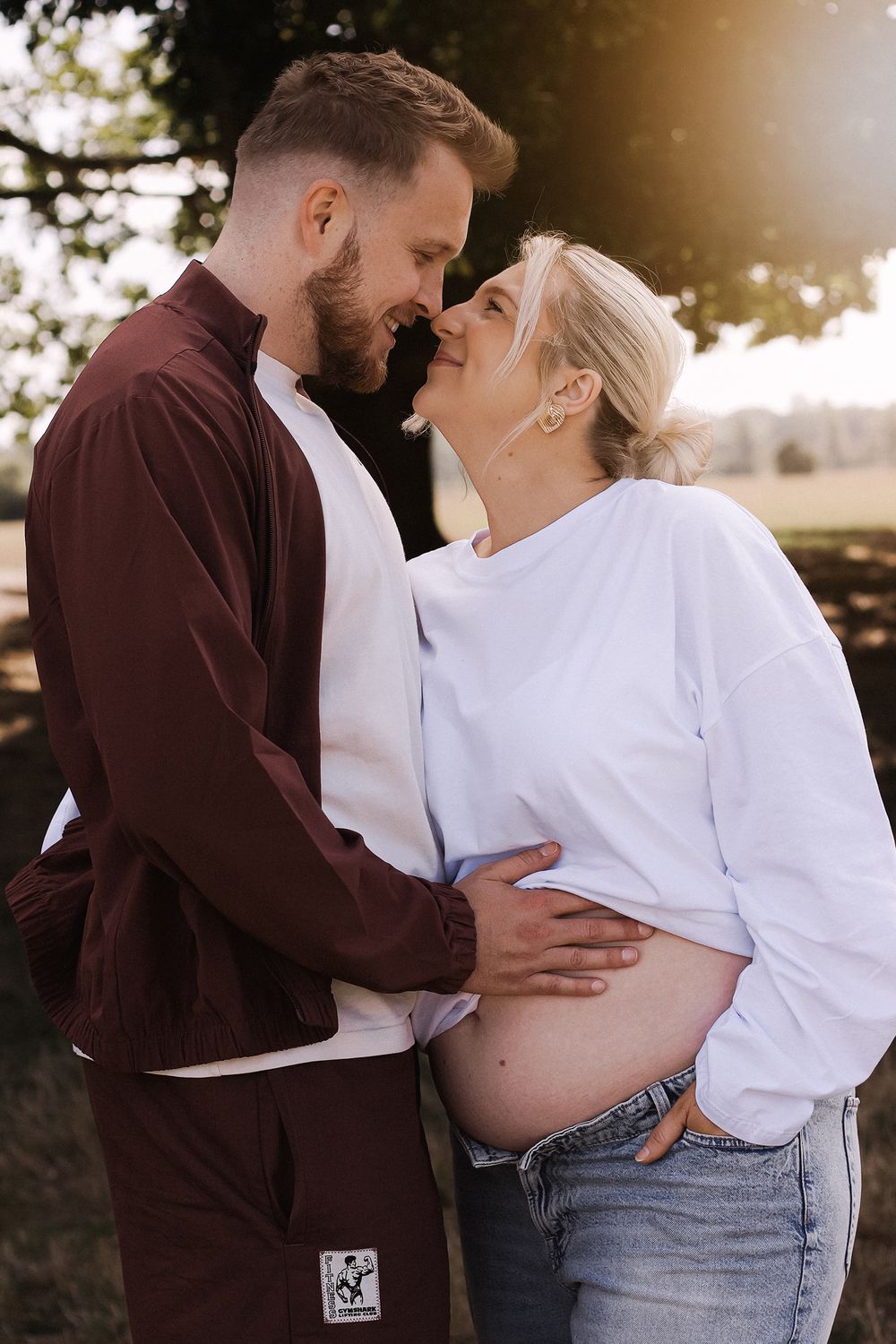 Expecting couple touching foreheads under a tree in golden evening light