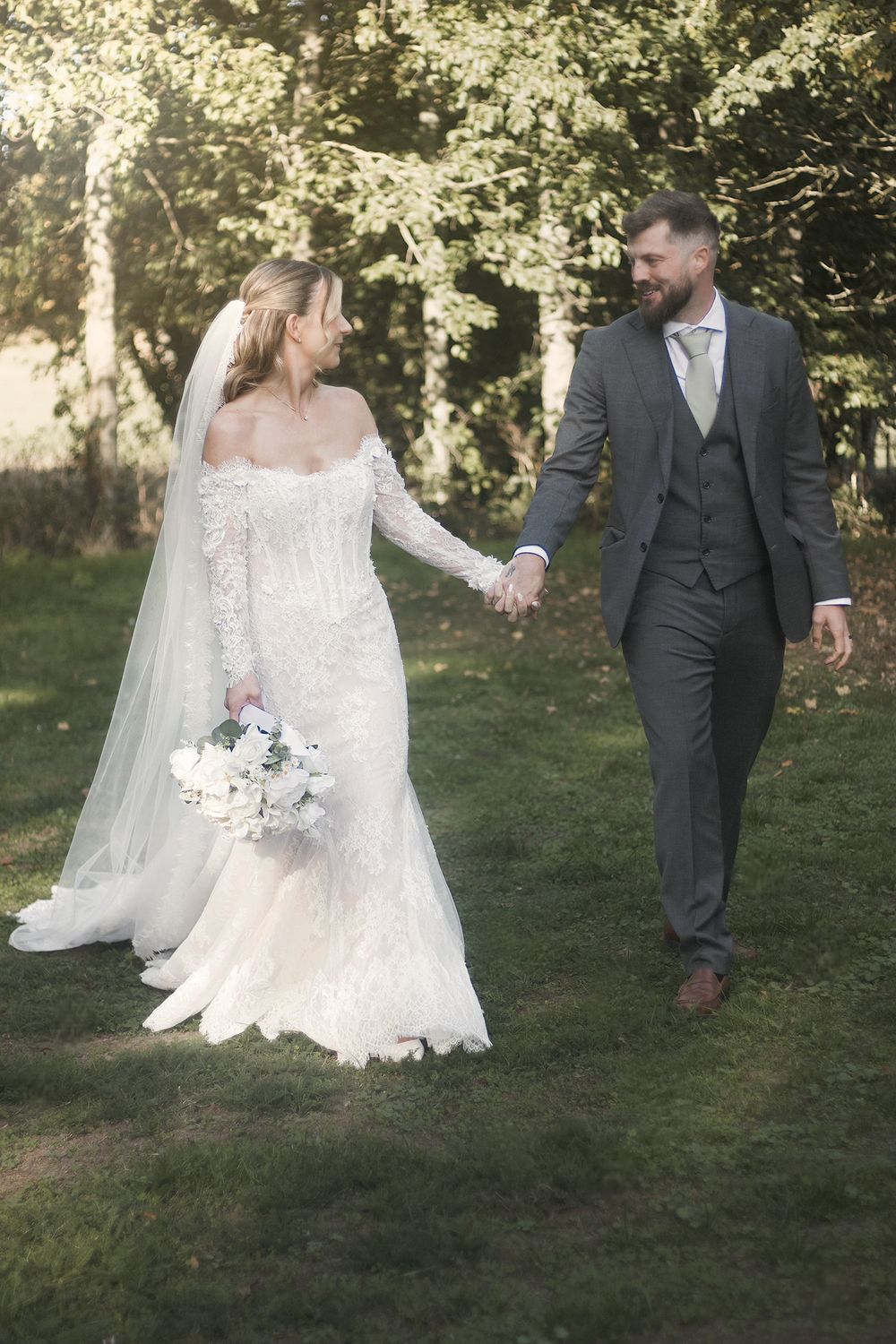 Bride and groom walking hand in hand across a lawn